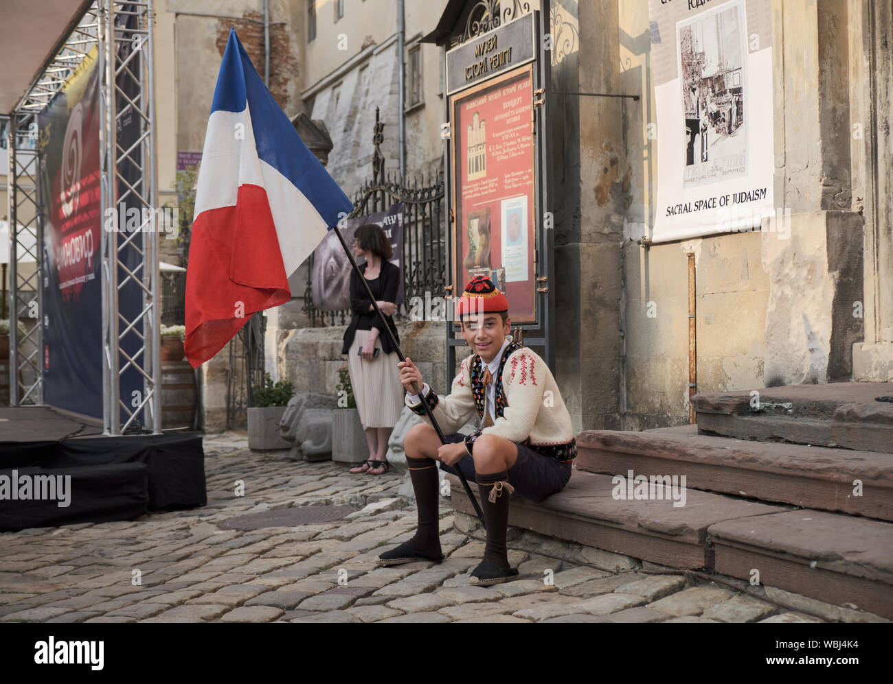 Portrait of young French boy dressed in couserans folkloric clothes sitting on step. Flag bearer for Parade of Etnovyr Festival in street of Lviv. Stock Photo