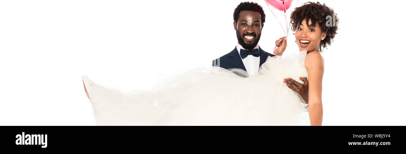 panoramic shot of handsome african american bridegroom holding in arms bride in wedding dress isolated on white Stock Photo