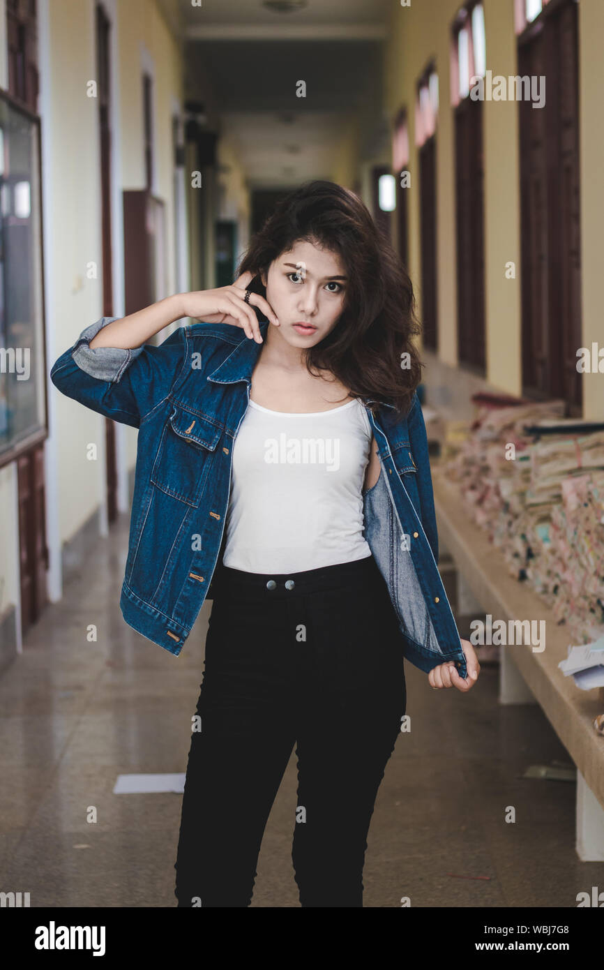 Portrait Of Young Woman Holding Denim Jacket While Standing In Corridor Stock Photo