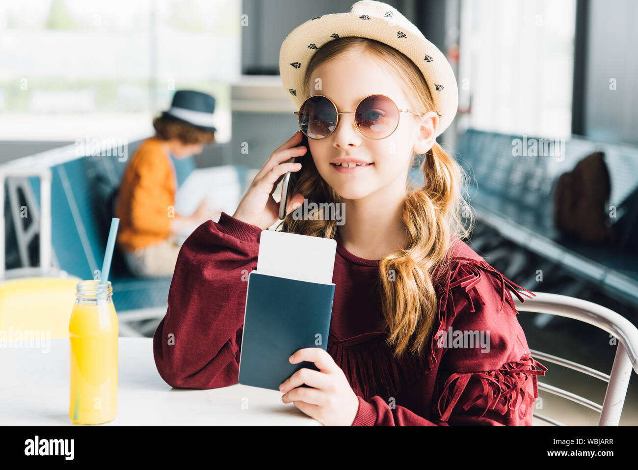 smiling preteen kid holding passport and talking on smartphone in waiting hall Stock Photo