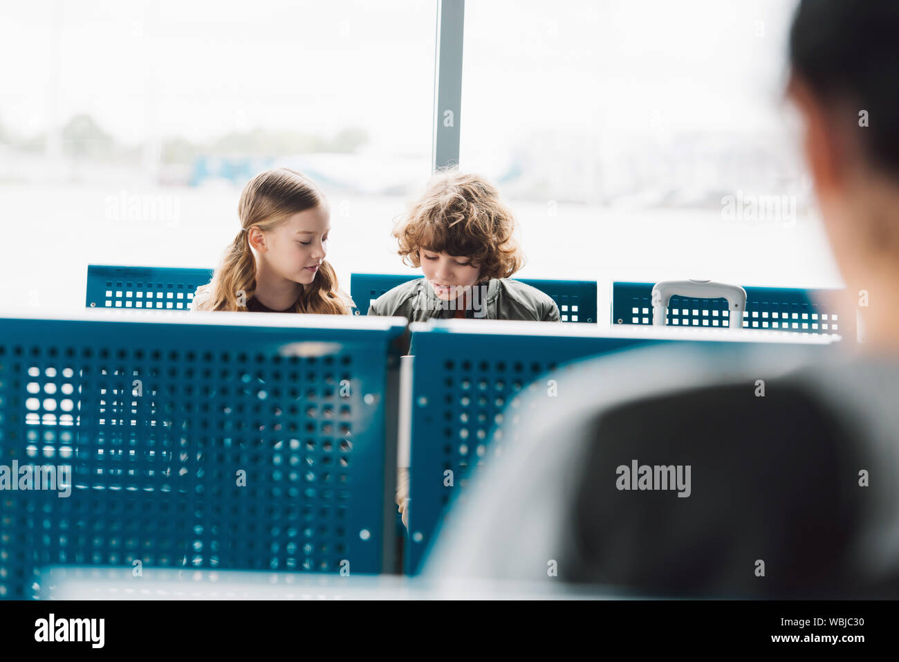 kids sitting and talking in waiting hall with blue seats in airport Stock Photo