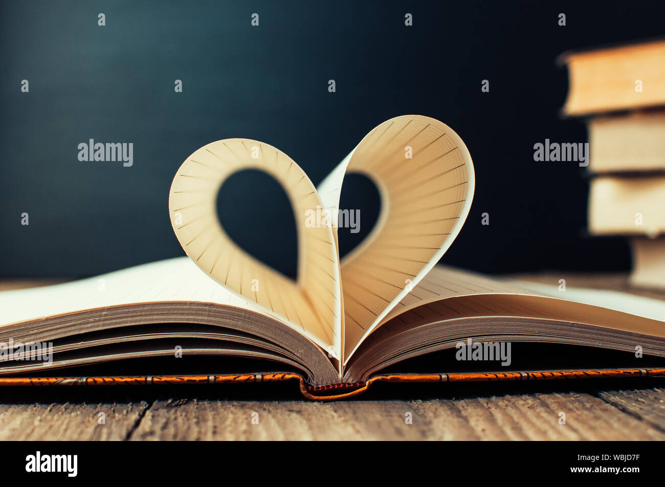 Sheets of a notebook in a cage wrapped in the shape of a heart.In the background is a stack of books and a black board.Education concept.Valentine's D Stock Photo