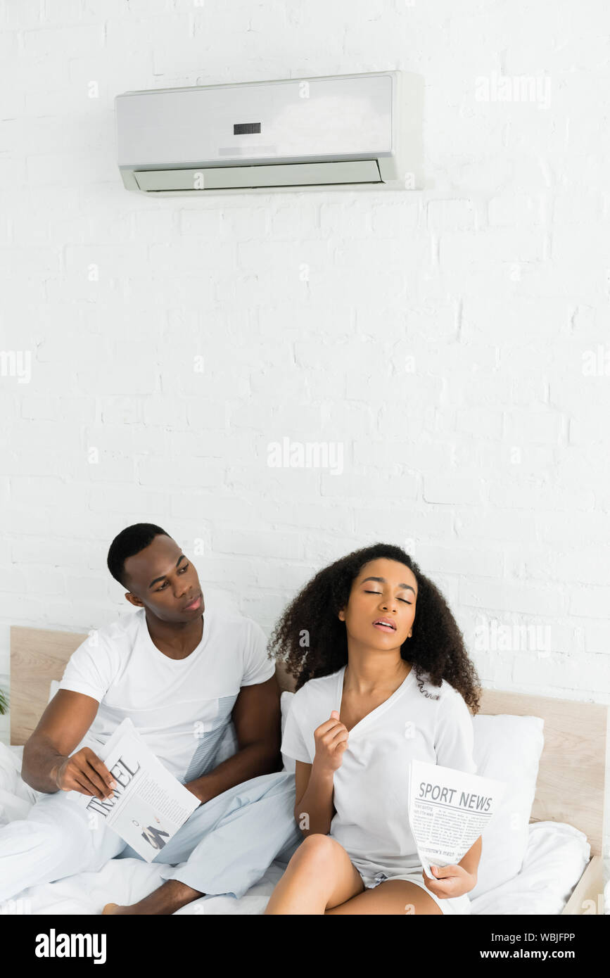 african american man looking at sweaty woman in room with air conditioner Stock Photo