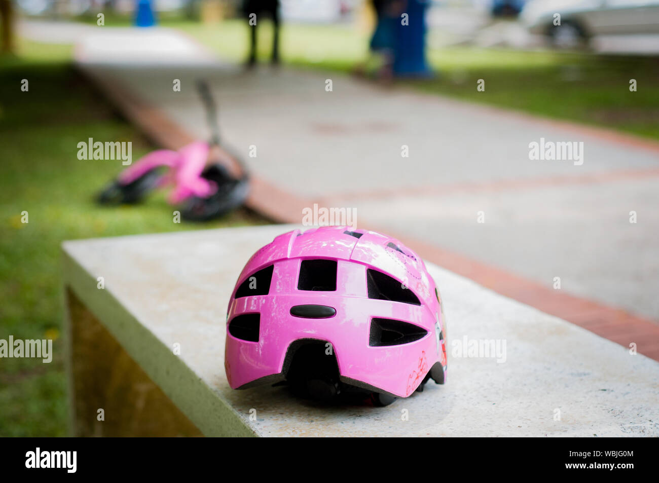 Pink helmet on the concrete bench in the park with pink pushbike in the background. Stock Photo