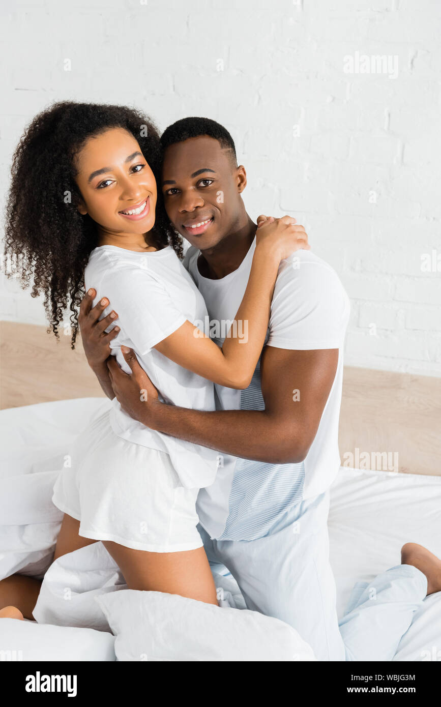 african american cuople standing on bed, hugging each other and looking ...