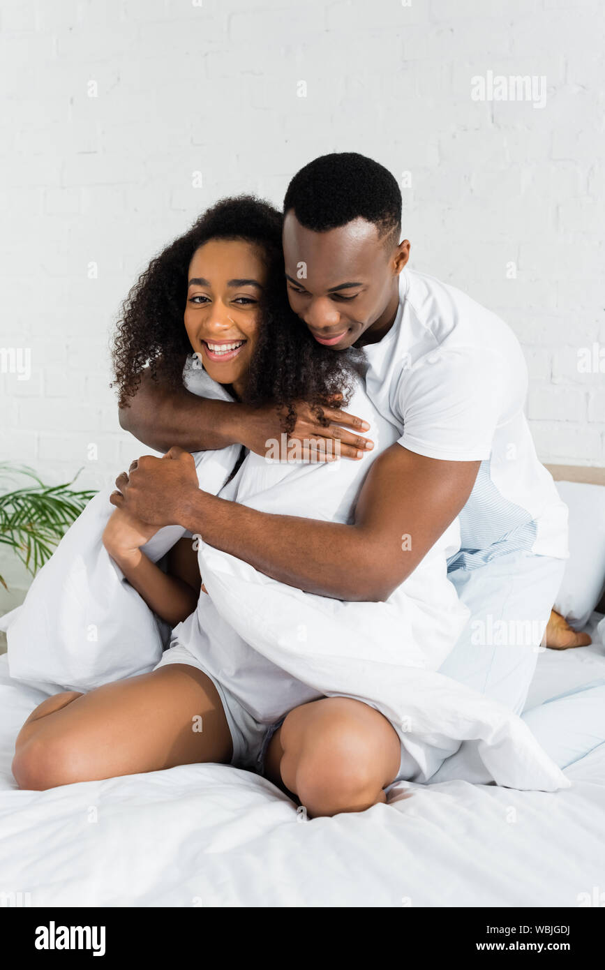 african american man hugging his charming girlfriend, sitting on white