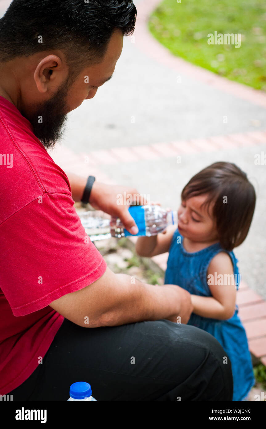 Bearded man gives water to a toddler child. Asian family, parenting and fatherhood concept. Stock Photo