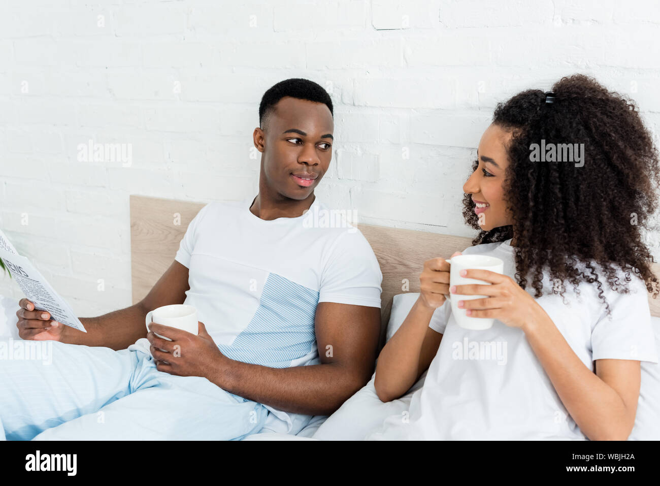 happy african american couple with newspaper and cup lying in bed ...
