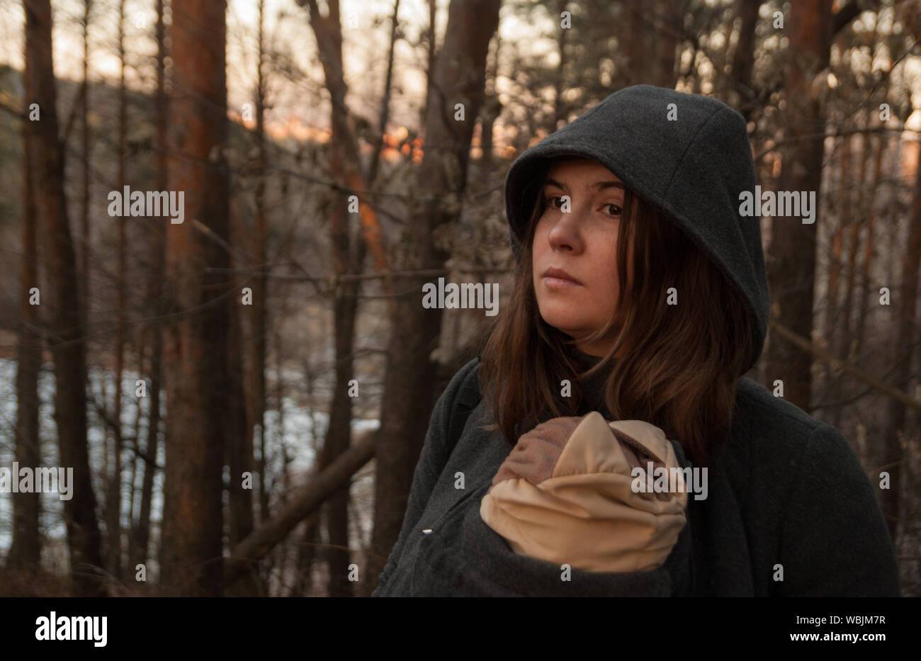 Woman With Baby In Sling Against Trees At Forest Stock Photo