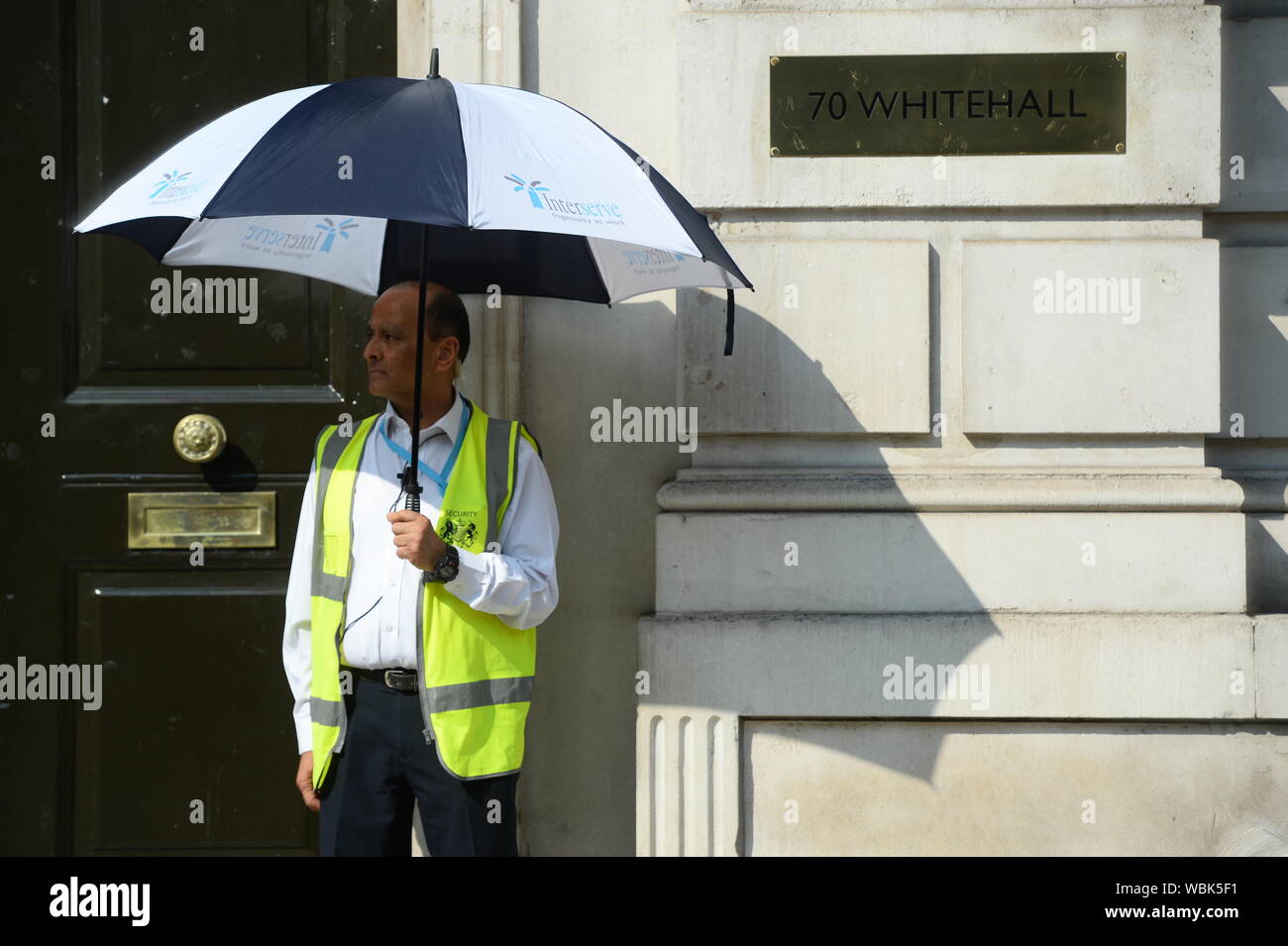 A security guard shades himself from the sun outside the Cabinet Office in London, ahead of today's cross party meeting looking at ways to stop a no deal Brexit. Stock Photo