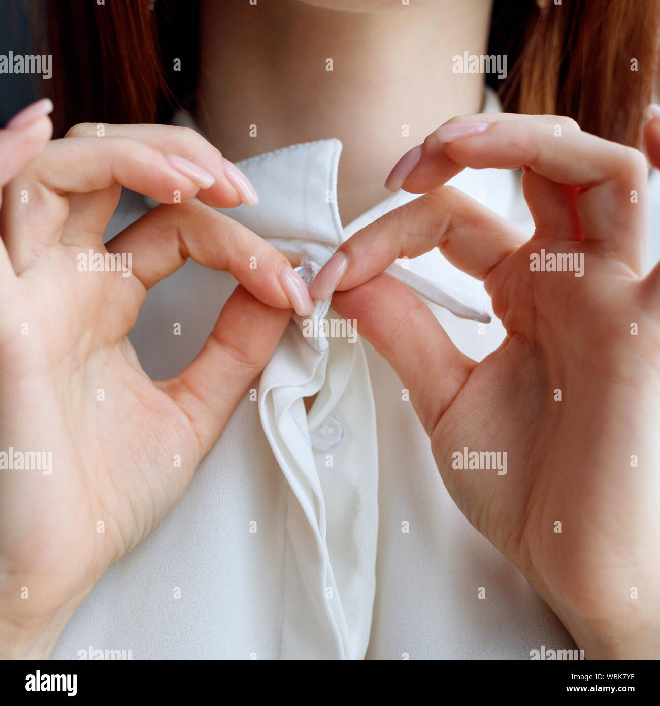 Unrecognizable redhead woman unbuttoning white blouse at home. Close-up view on hands. Stock Photo