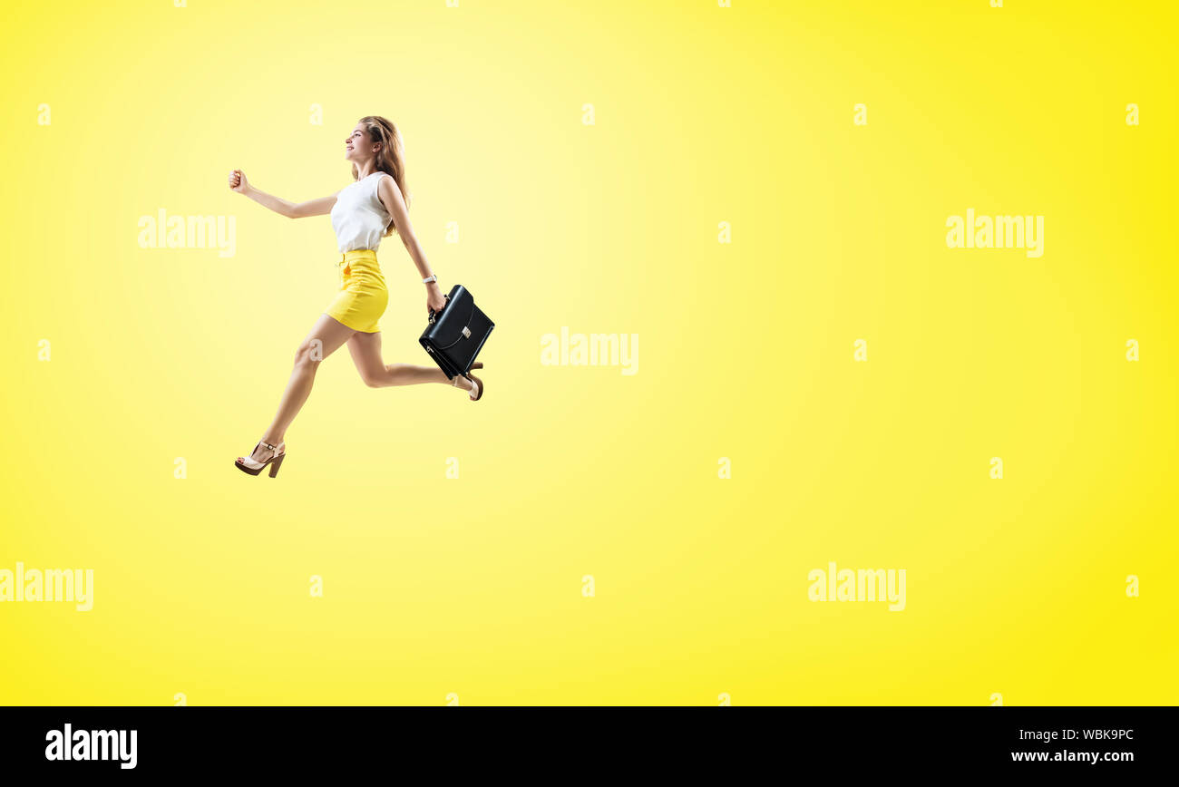 Young cheerful woman running fast with briefcase. Over bright yellow background. Stock Photo