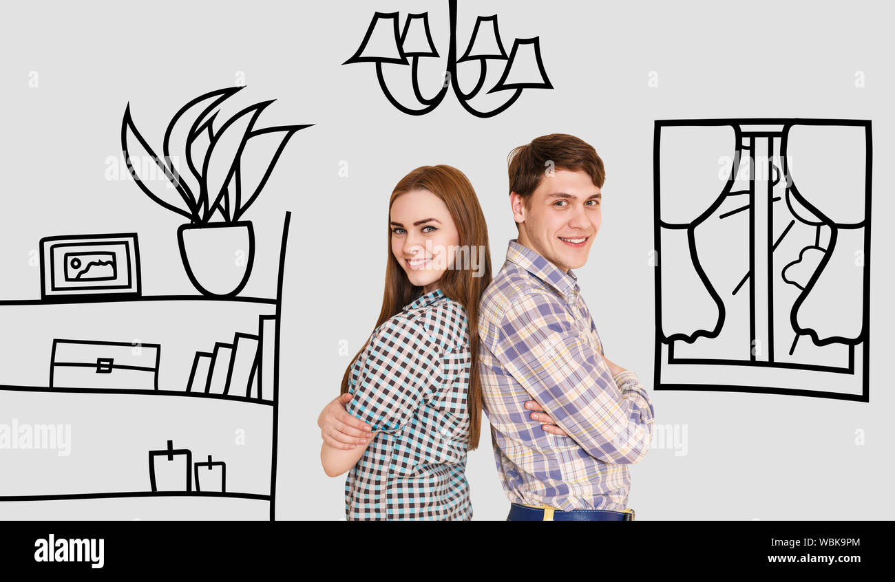 Young happy couple stands back to back in their new flat among painted furniture on the wall. Stock Photo