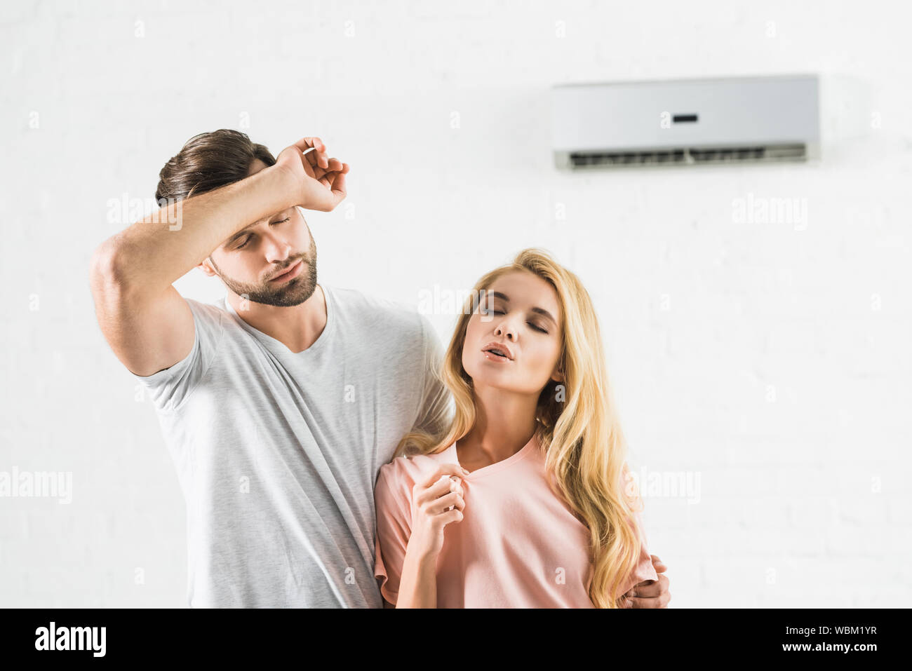 couple wiping forehead and suffering from heat under air conditioner at home Stock Photo