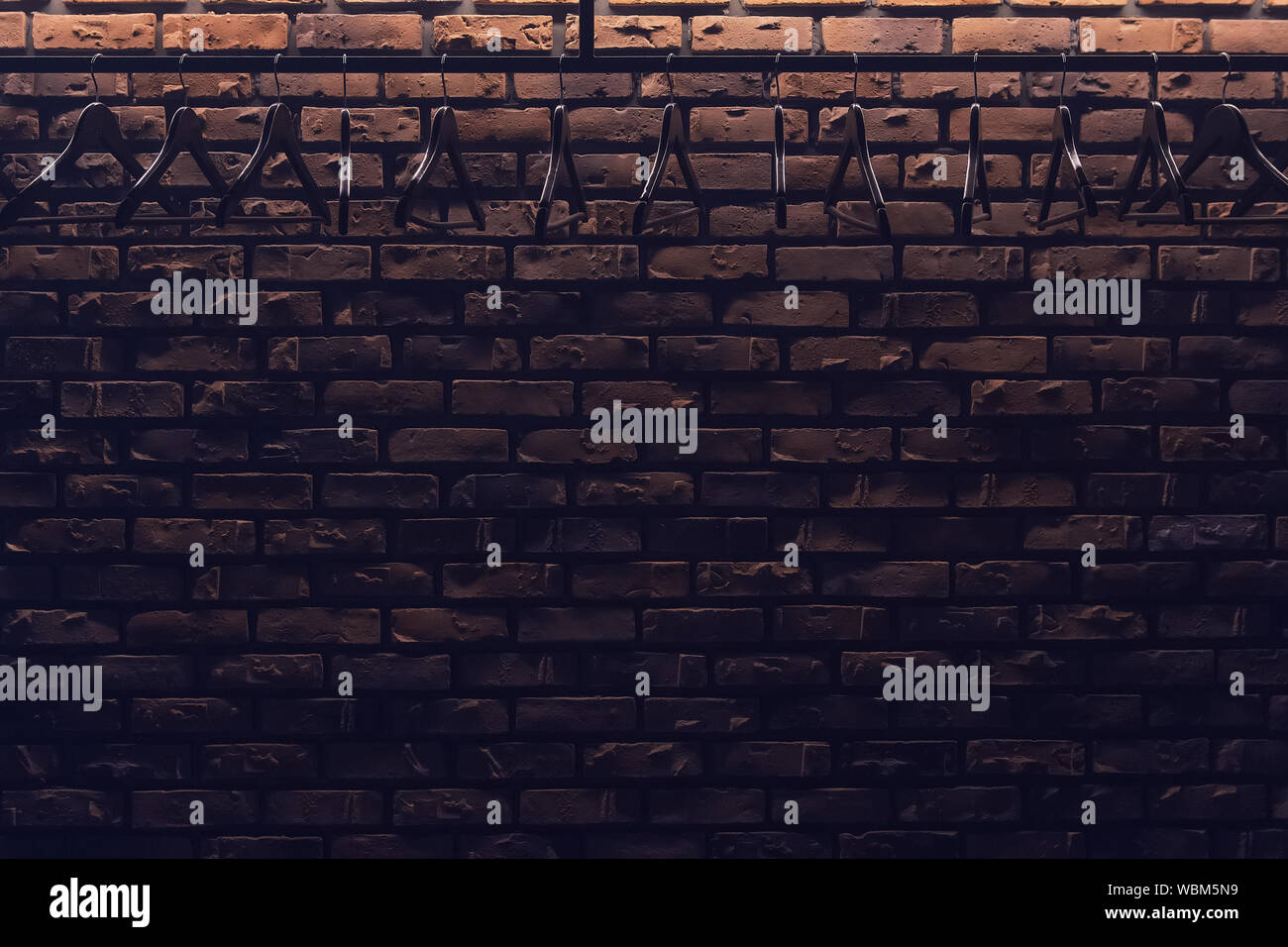 A lot of wooden coat hangers hanging in the night club with low light. Uneven brick wall on the background. Empty bar with no visitors. Copy space. Stock Photo