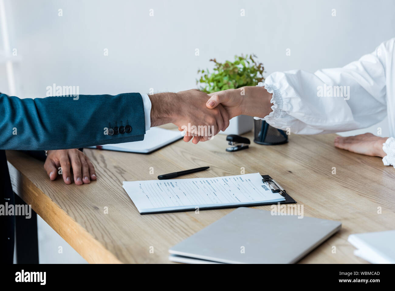 cropped view of recruiter and woman shaking hands near clipboard on table Stock Photo