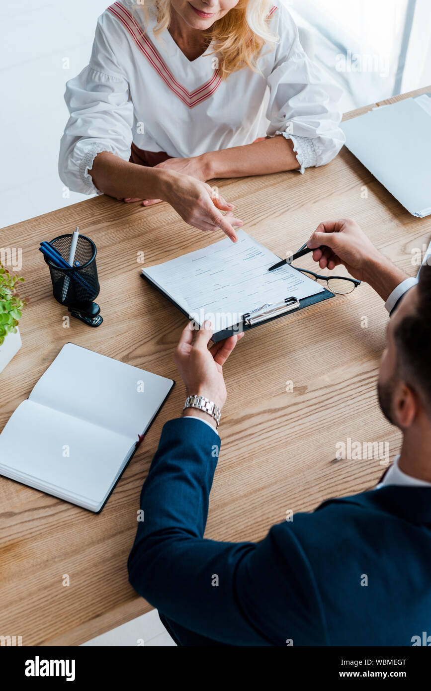 overhead view of blonde employee pointing with finger at clipboard near recruiter Stock Photo