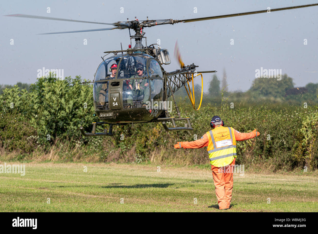 Aérospatiale Alouette II helicopter landing at the Children in Need Little Gransden Air and Car Show. Marshaller lowering to land arm signal Stock Photo