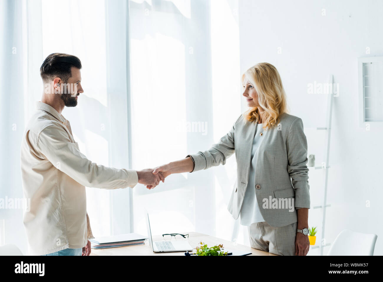 attractive blonde recruiter and handsome employee shaking hands Stock Photo