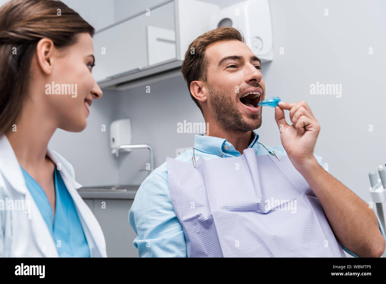 selective focus of patient putting retainer in mouth near happy dentist