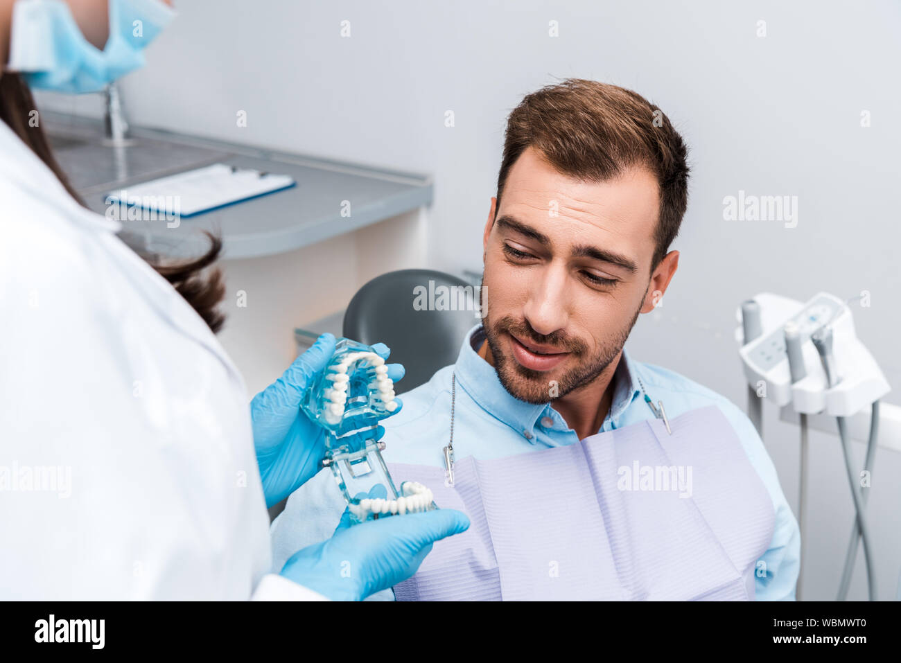 cropped view of dentist in medial mask and latex gloves holding teeth model near handsome patient Stock Photo