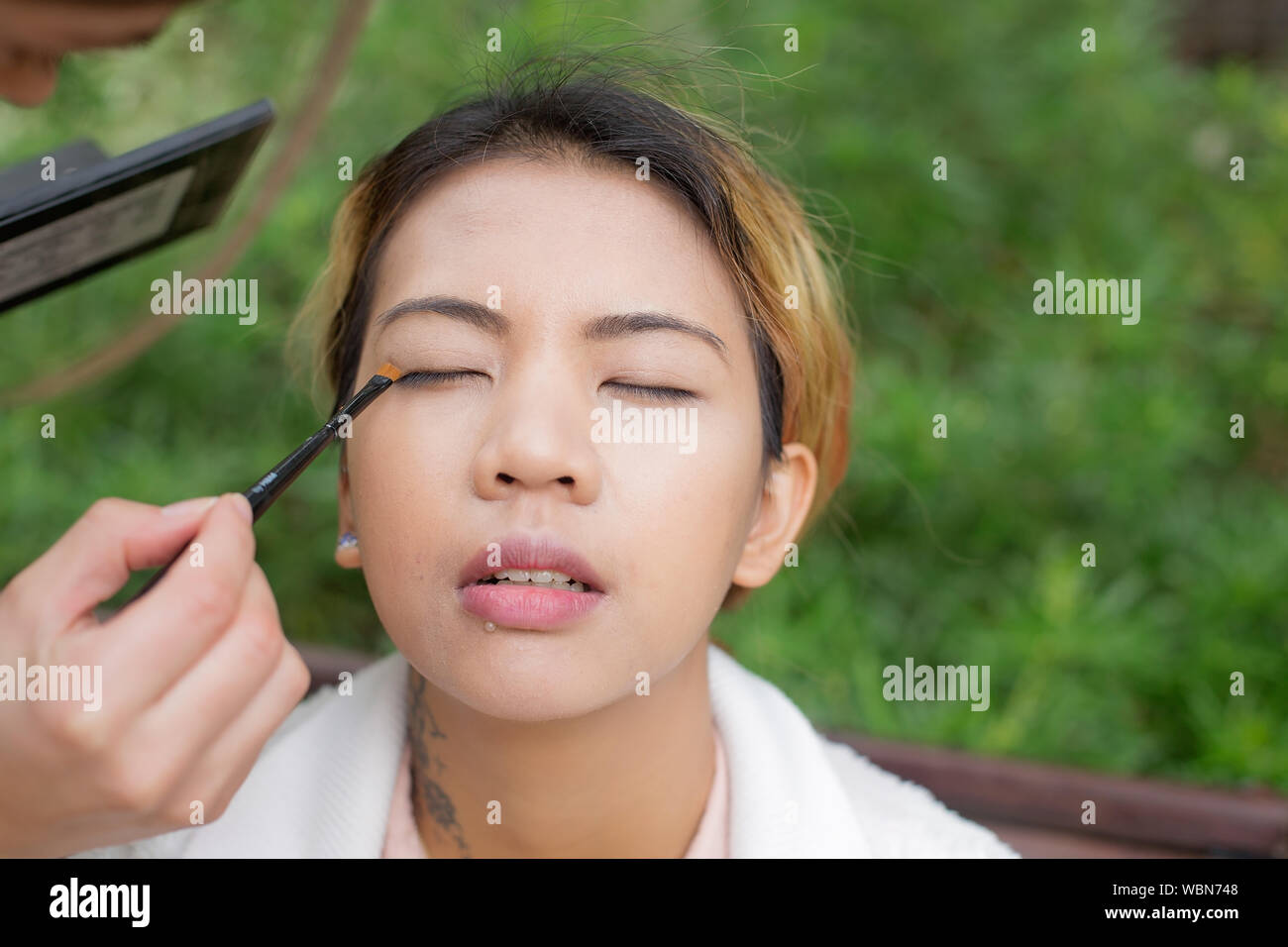 Close up of a female Asian model while applying makeup to her eyes closed Stock Photo