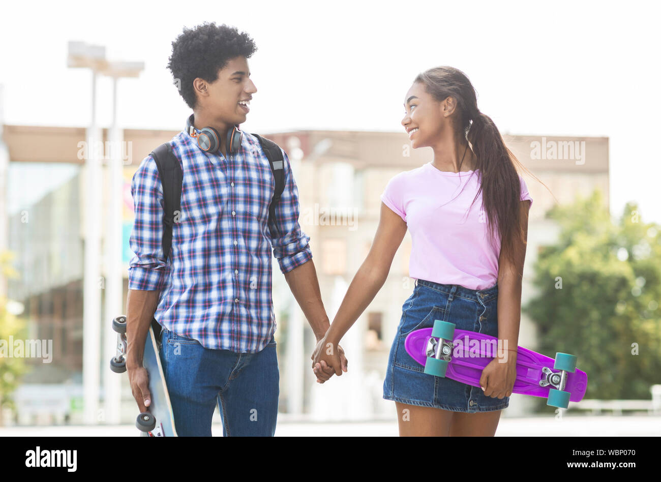 Teenage couple with skateboards holding hands walking along city street Stock Photo