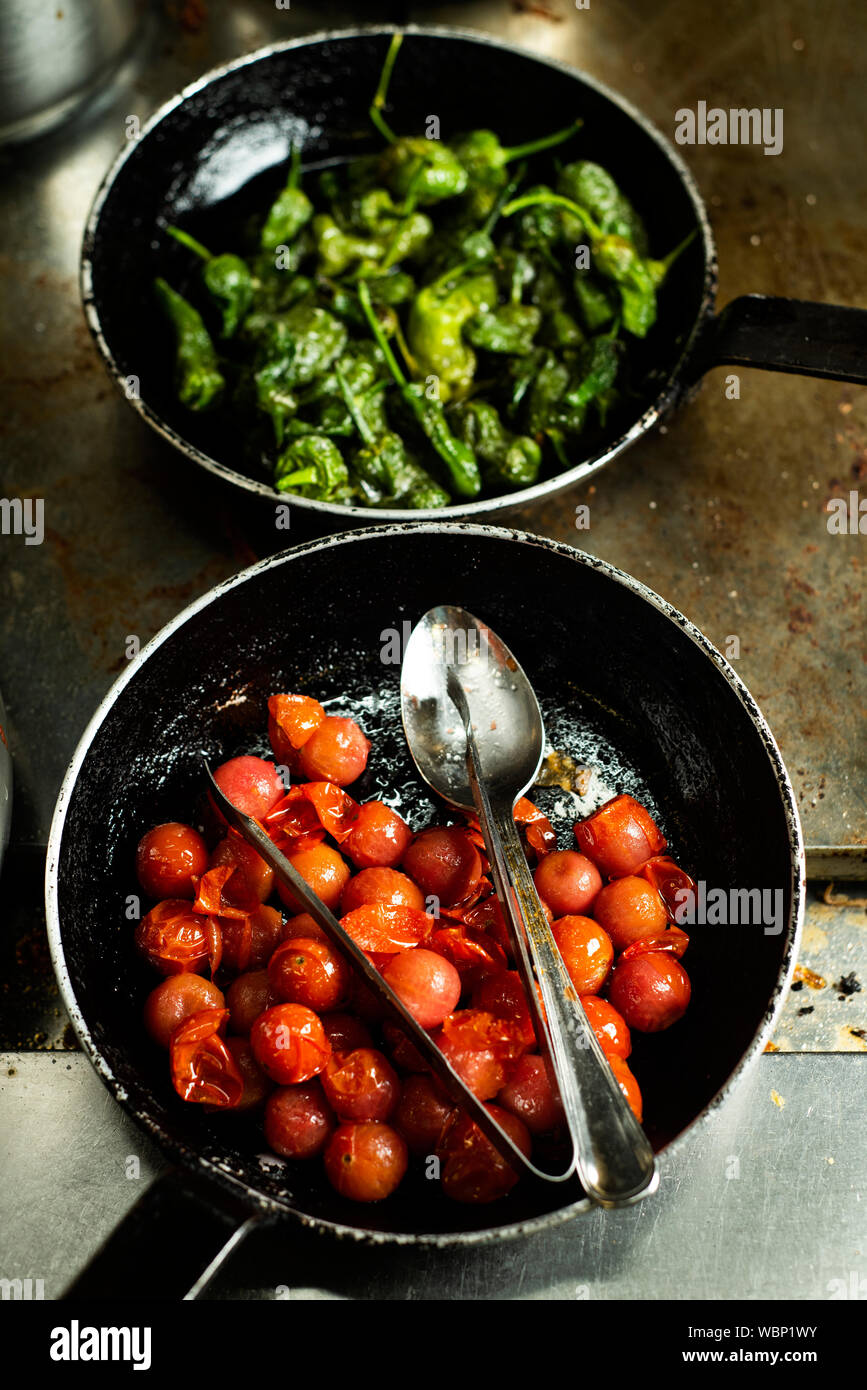 closeup of some cooked cherry tomatoes and green peppers in different frying pans in a professional kitchen Stock Photo