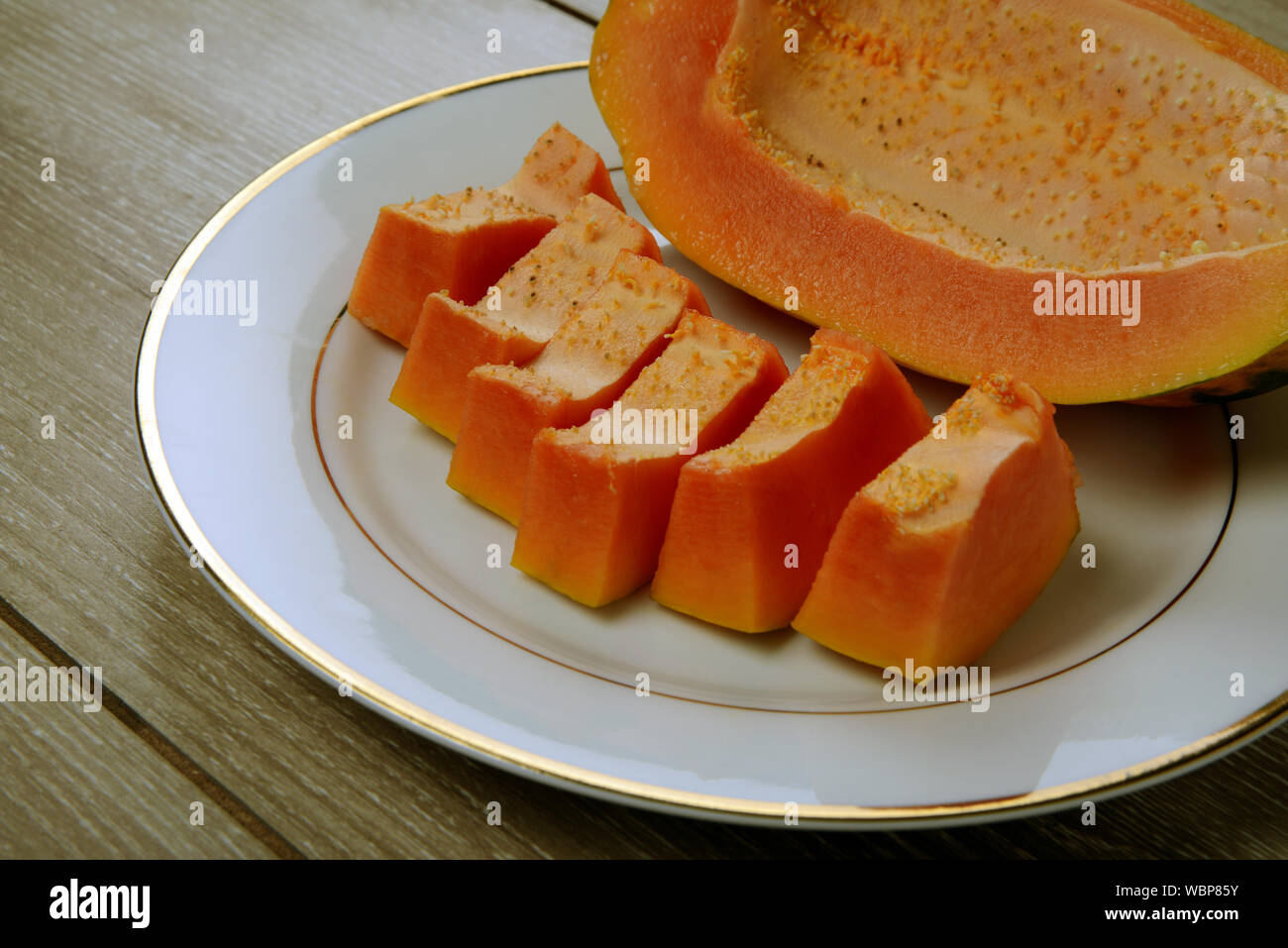 Ripe Seedless Papaya fruit pieces in a white plate on wooden background Stock Photo