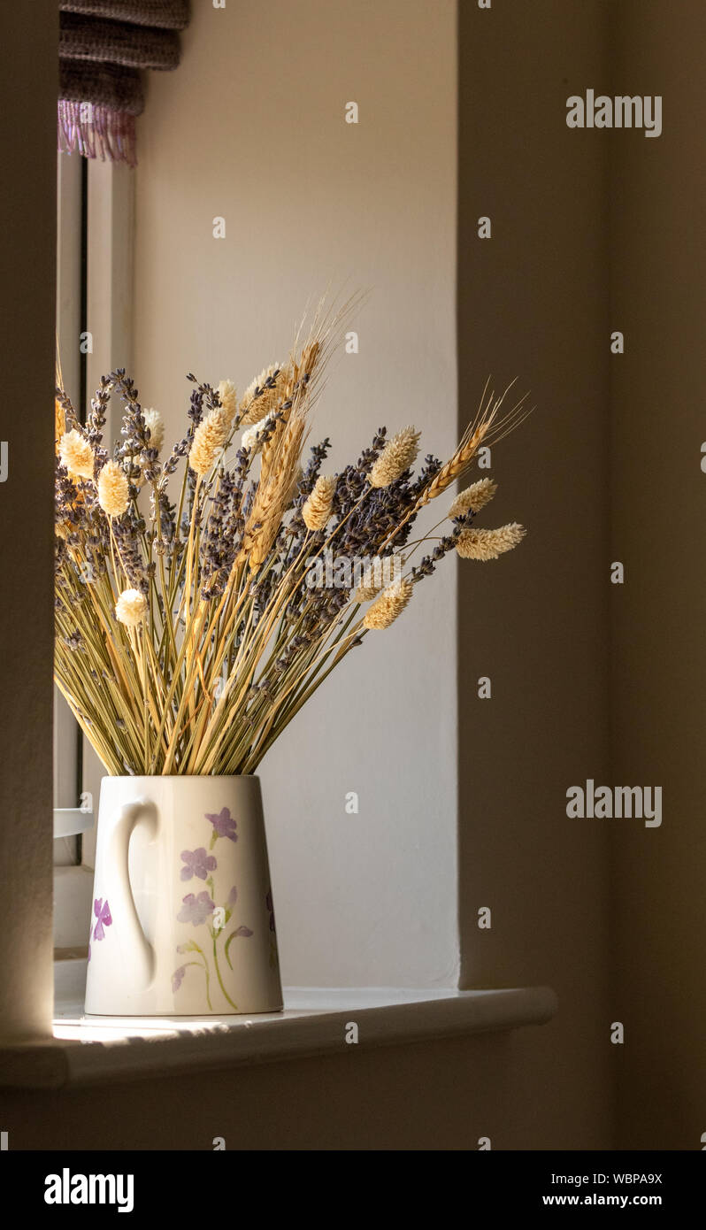 A jug of dried lavender and grasses on a window sill. The light source is natural sunlight coming through the window. Stock Photo