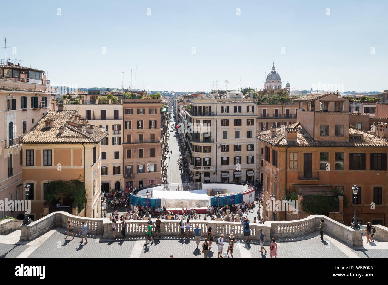A crowd of tourists walking and sightseeing Piazza Spagna Rome in a summer sunny day.  Restoration and preservation work for the fountain can be seen Stock Photo