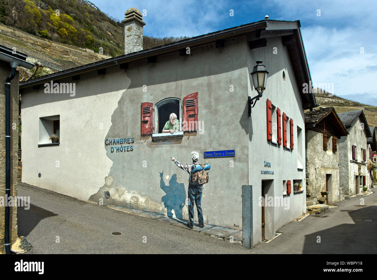 Hiker looking for acomodation speaks to a landlady,Trompe-l’œil painting at a house, Branson, Valais, Switzerland Stock Photo