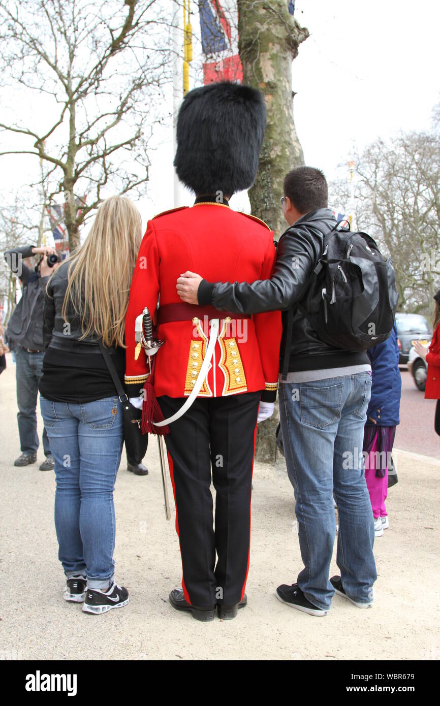 TOURISTS TO LONDON SURROUND A WELSH GUARDS OFFICER IN THE MALL NEAR BUCKINGHAM PALACE AND ARE HAVING ALOT OF FUN INTERACTING WITH HIM. WELSH GUARDS REGIMENT. BRITISH SOLDIERS. GUARDS UNIFORM. THE HEADWEAR OF THE FIVE BRITISH GUARDS REGIMENTS IS CALLED A BUSBY OR BEARSKIN. LONDON IS A VERY POPULAR TOURIST DESTINATION WITH 51% OF THE 39 MILLION VISITORS TO THE UNITED KINGDOM IN 2017. CEREMONIAL MILITARY UNIFORM. BEARSKIN CAP. BRITISH ARMY. TRAVEL IN THE UK. TRAVEL. CITY BREAKS. CIVILIZED SOCIETY. SAFEST CITIES. Stock Photo