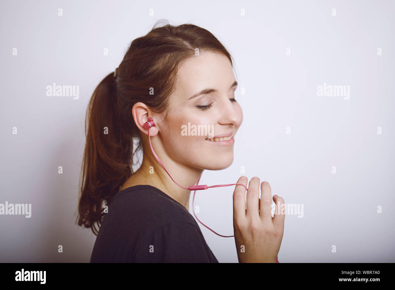 Young Woman Holding In-ear Headphones Over White Background Stock Photo