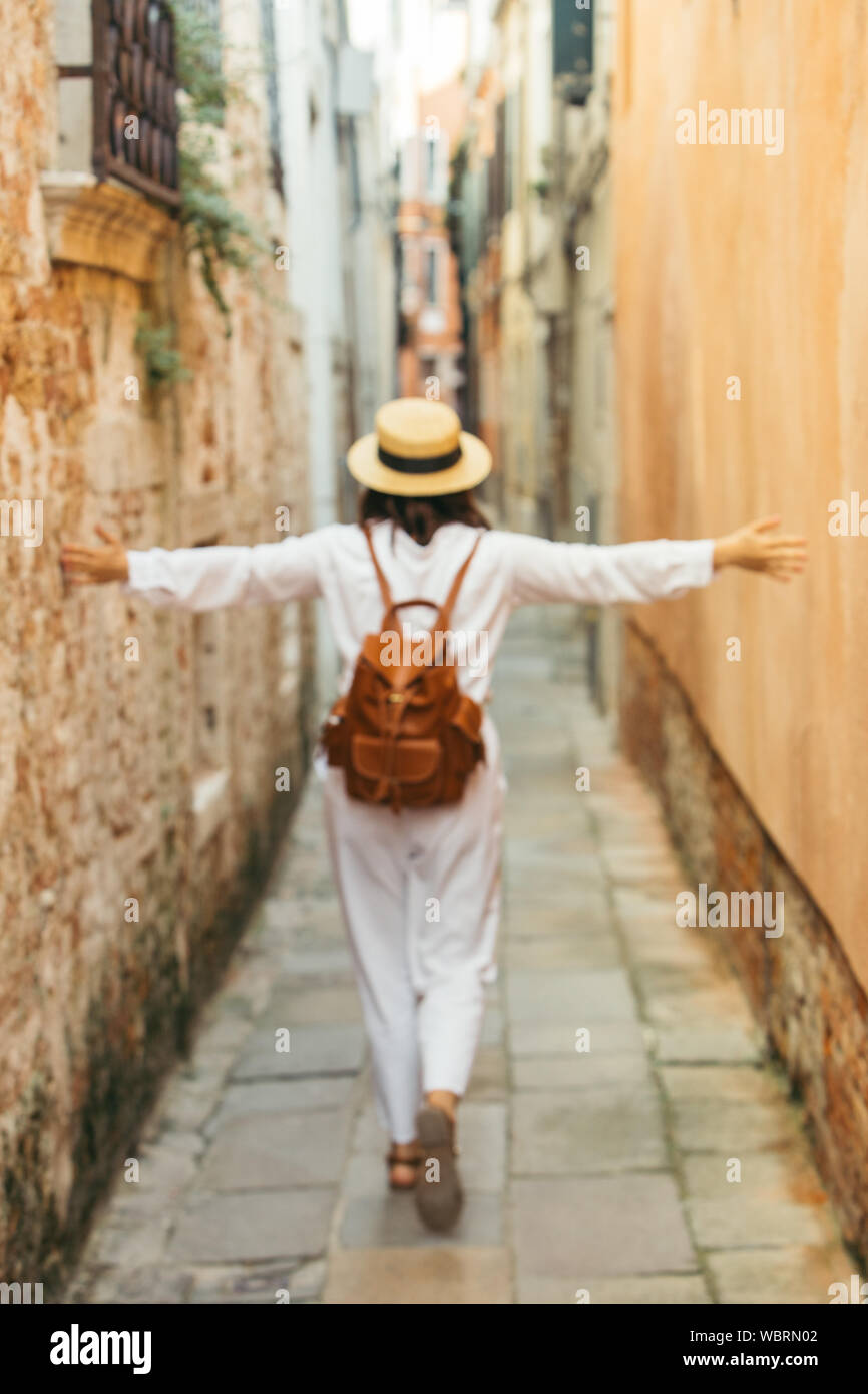 woman in white clothes in straw hat and brown leather backpack walking by city street Stock Photo