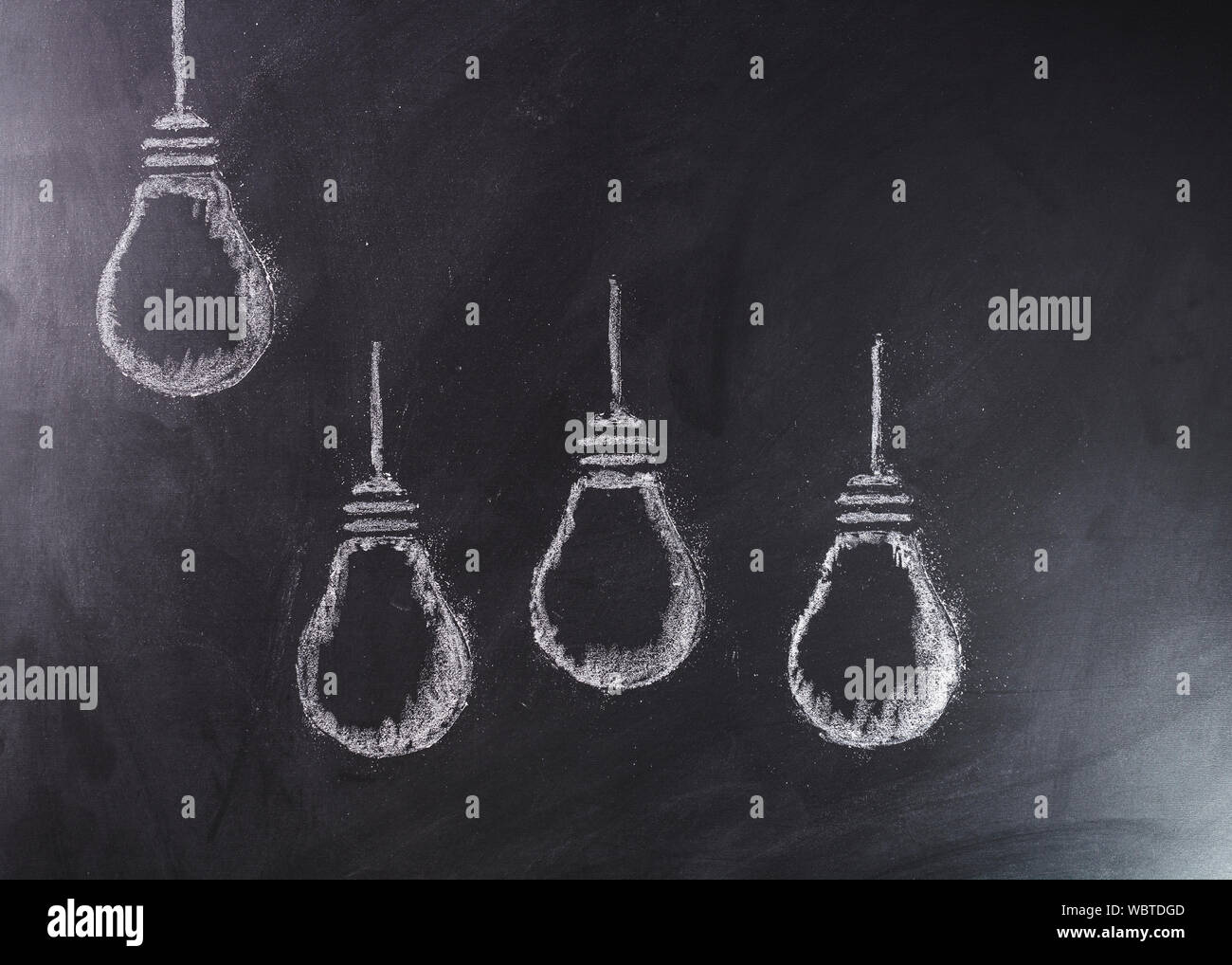 Light bulbs sketched in white chalk with one elevated above the group. Stock Photo