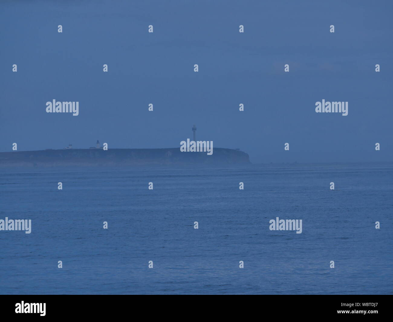 photo de l'île de ouessant dans la brume avec une mer calme avec au bout de l'île , la tour radar de ouessant et ses falaises abruptes . Stock Photo