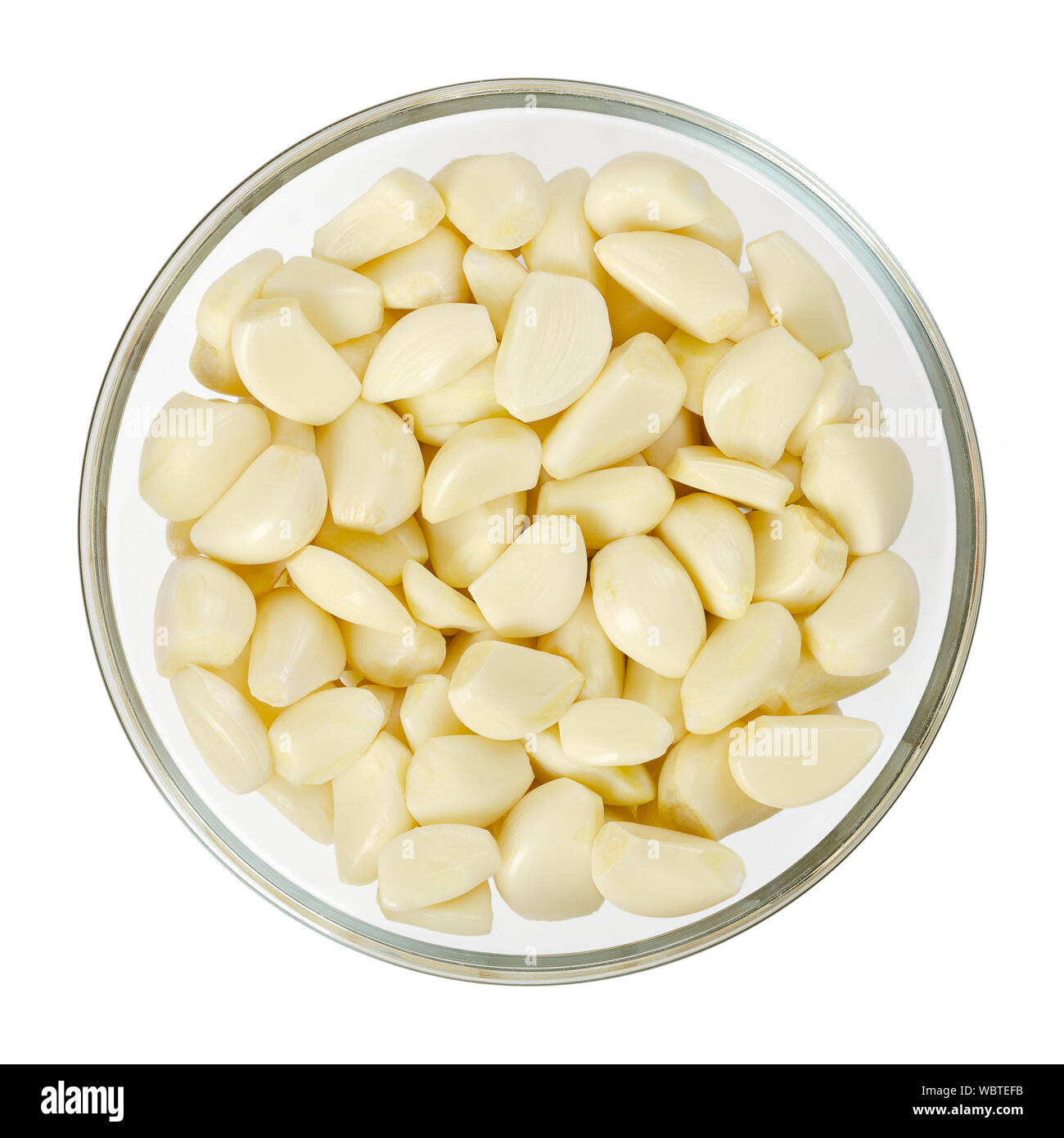 Peeled garlic cloves in glass bowl, from above. Allium sativum, with pungent flavor, used as seasoning or condiment and in medicine. Stock Photo