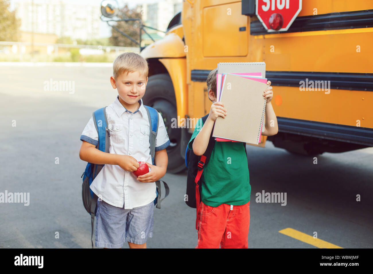 Two funny happy Caucasian boys students kids with apples standing near yellow bus on 1 September day. Education and back to school concept. Children p Stock Photo