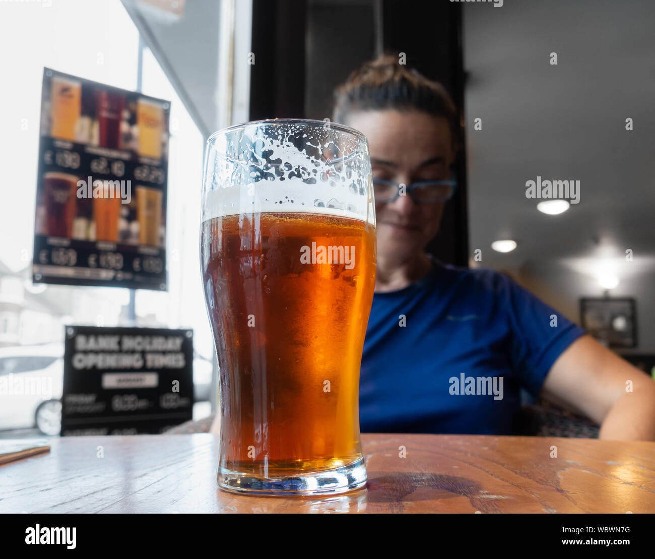 Woman with pint of beer, craft ale, looking at mobile phone in pub in England. UK Stock Photo