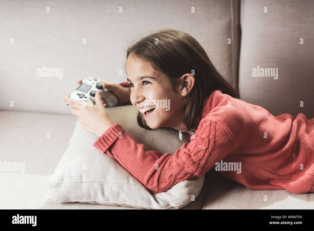 Niña jugando con la consola de videojuego en el sofá de la sala de estar de casa Stock Photo