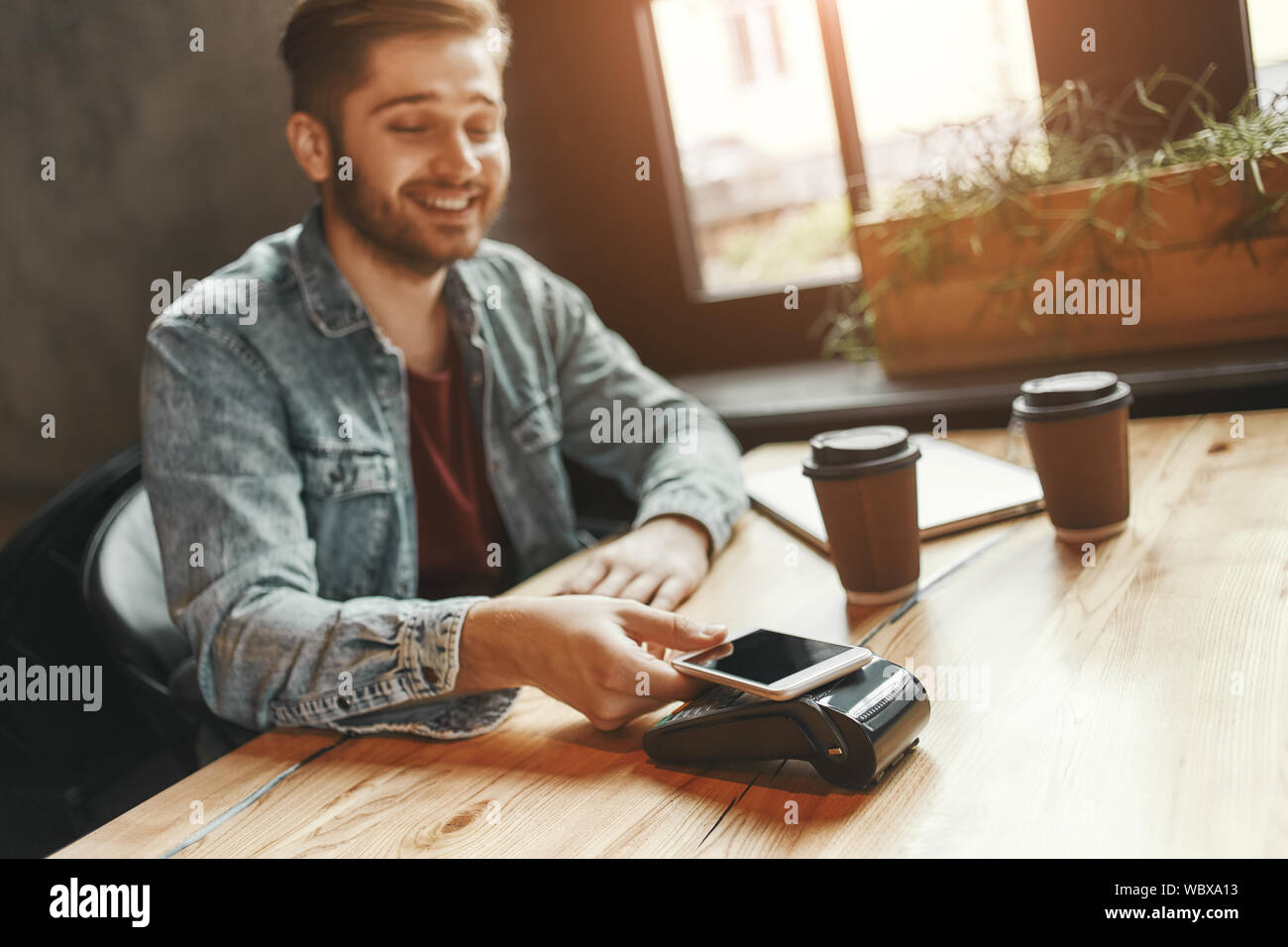 Portrait of young man paying bill through smartphone using NFC ...