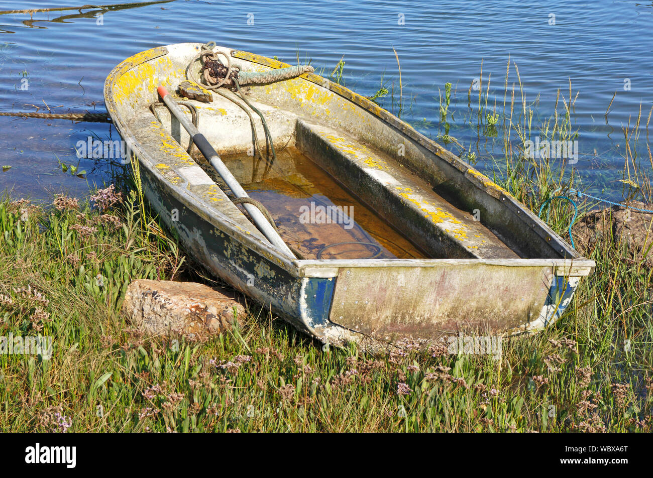 An old weathered dinghy on the bank by the side of the tidal channel at the east end of Wells-next-the-Sea, Norfolk, England, United Kingdom, Europe. Stock Photo