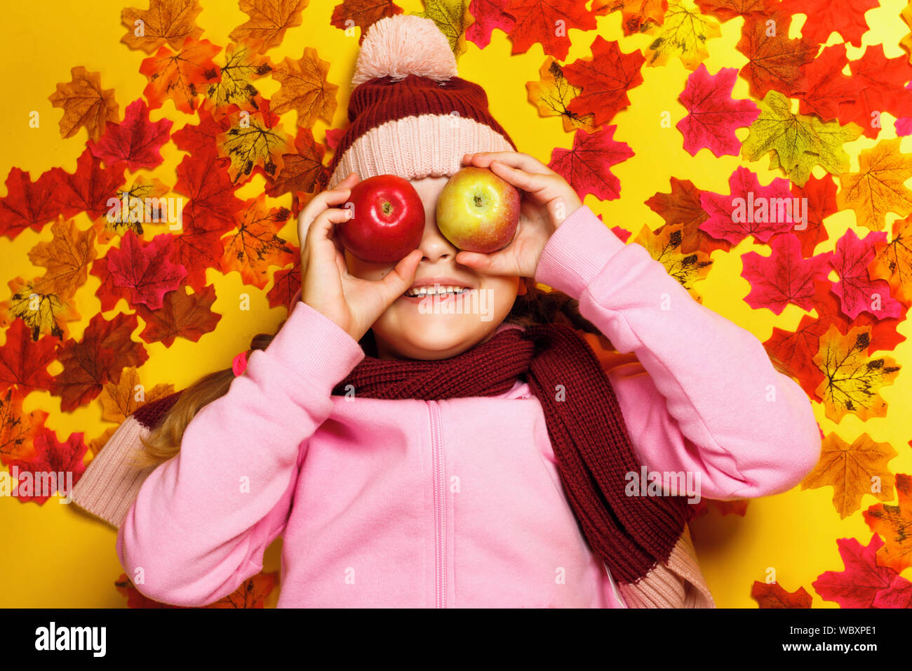 Top view of a happy little girl lying on autumn leaves. A child in a scarf and hat. Stock Photo
