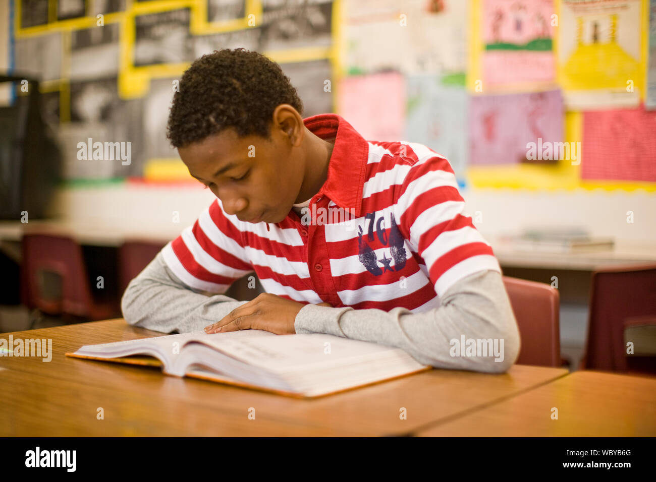 Teenage boy reading a book inside a classroom Stock Photo - Alamy