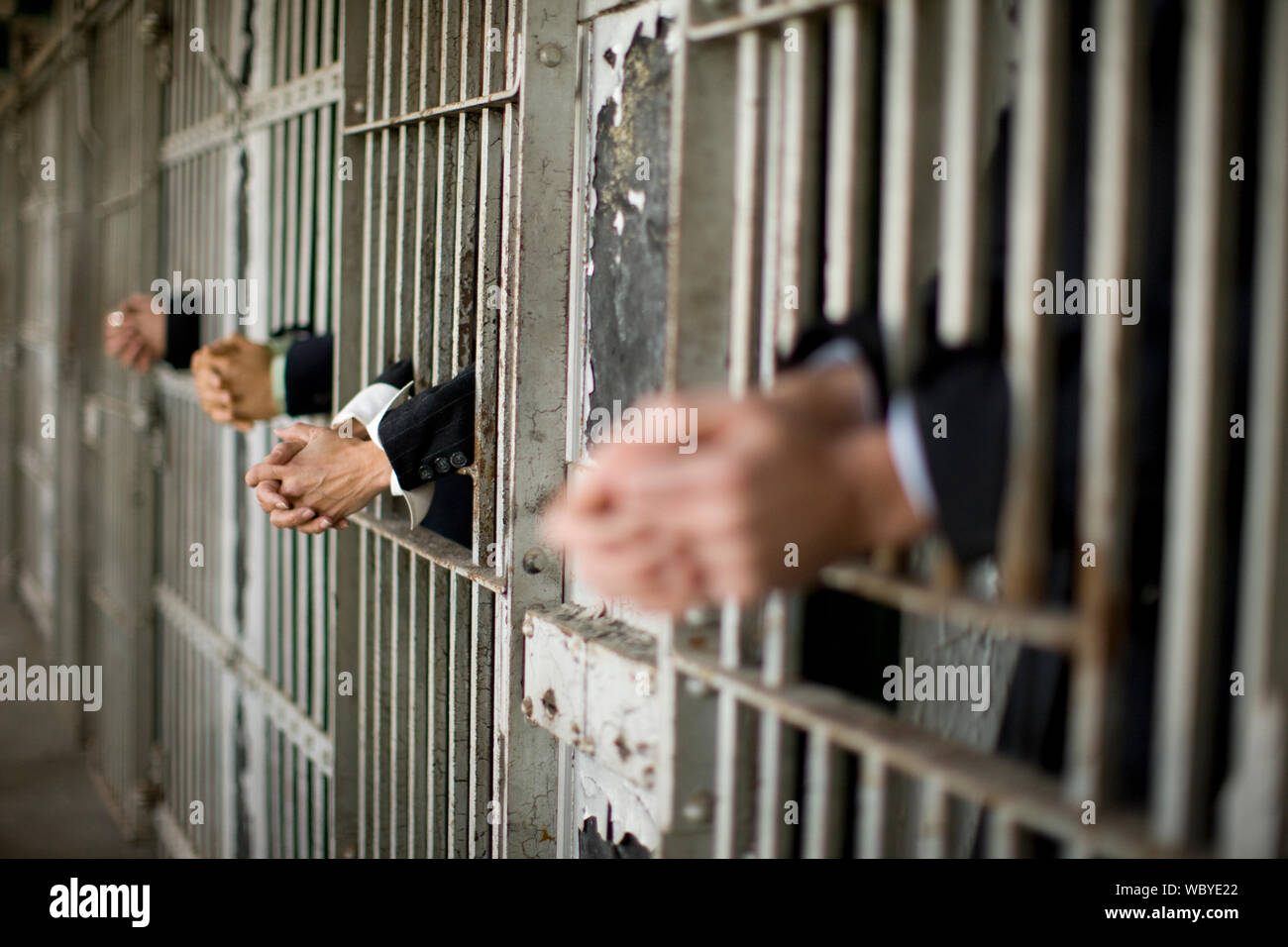 Hands of a mid-adult business woman and three colleagues through bars of a prison cell in a derelict building. Stock Photo