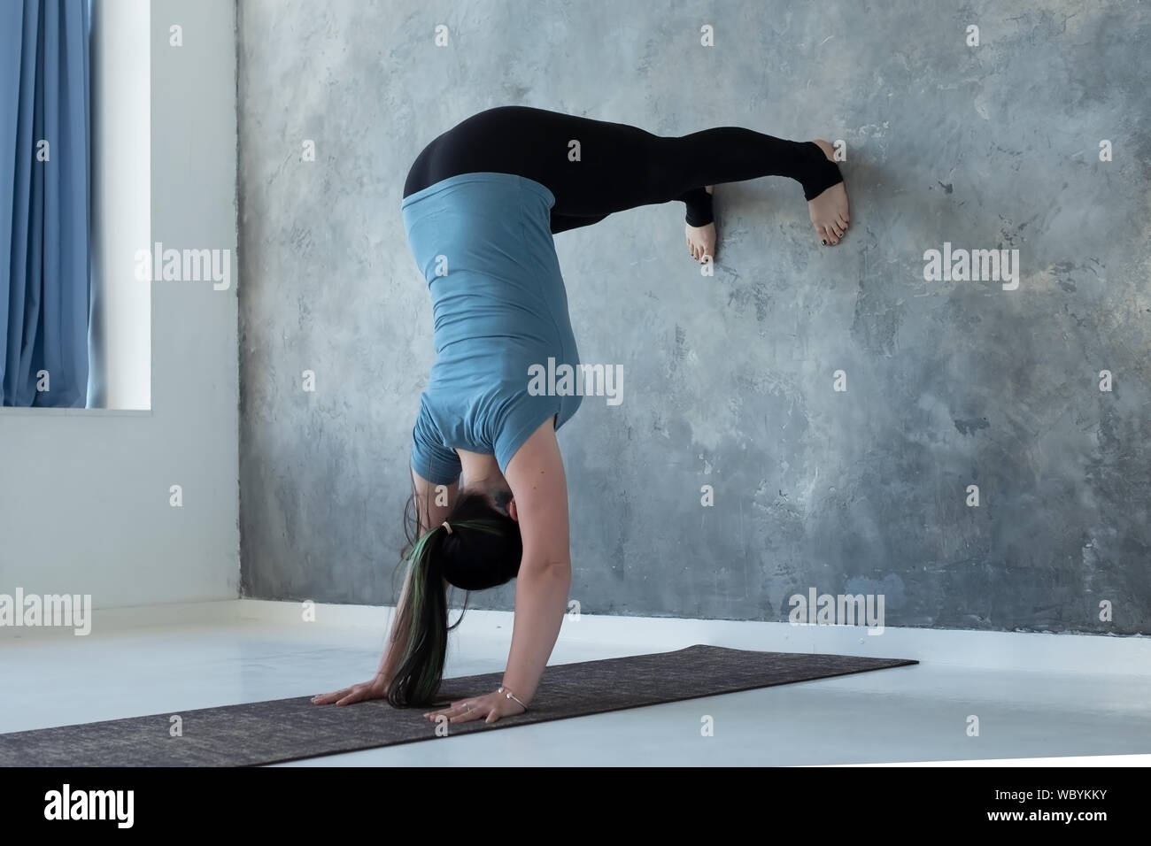 Woman learning to stand on hands near wall. Upside down yoga position. Studio shot Stock Photo