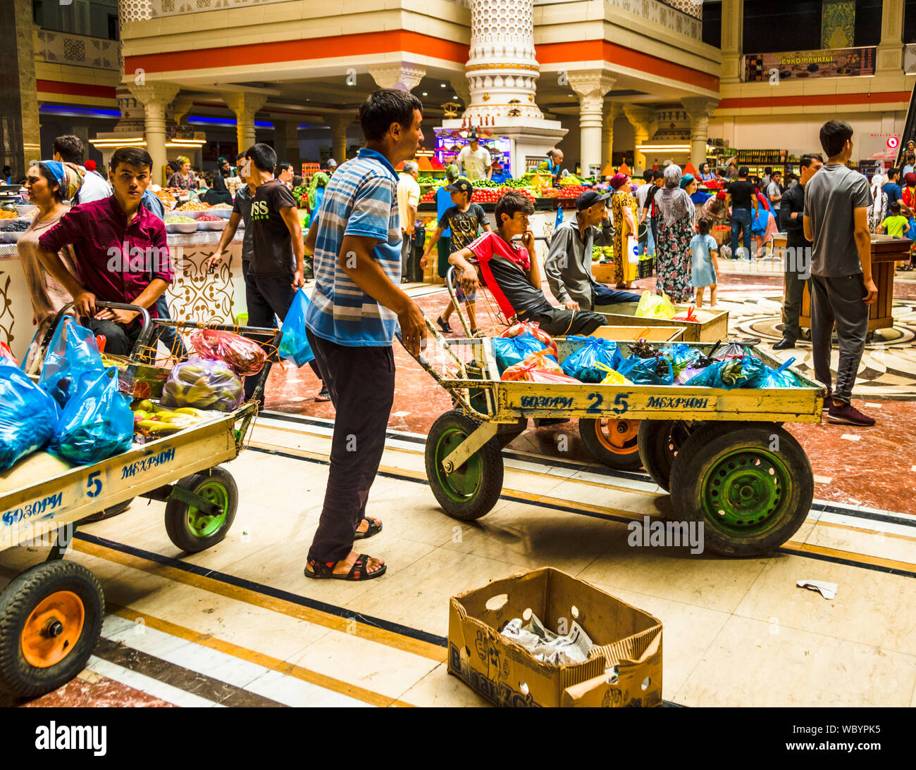 Handcarts labeled "Bozori Mehrgon" wait with their porters in the entrance hall of the Mehrgon market hall in Dushanbe, Tajikistan, ready for customers who want their purchases carried out to the car. Stock Photo