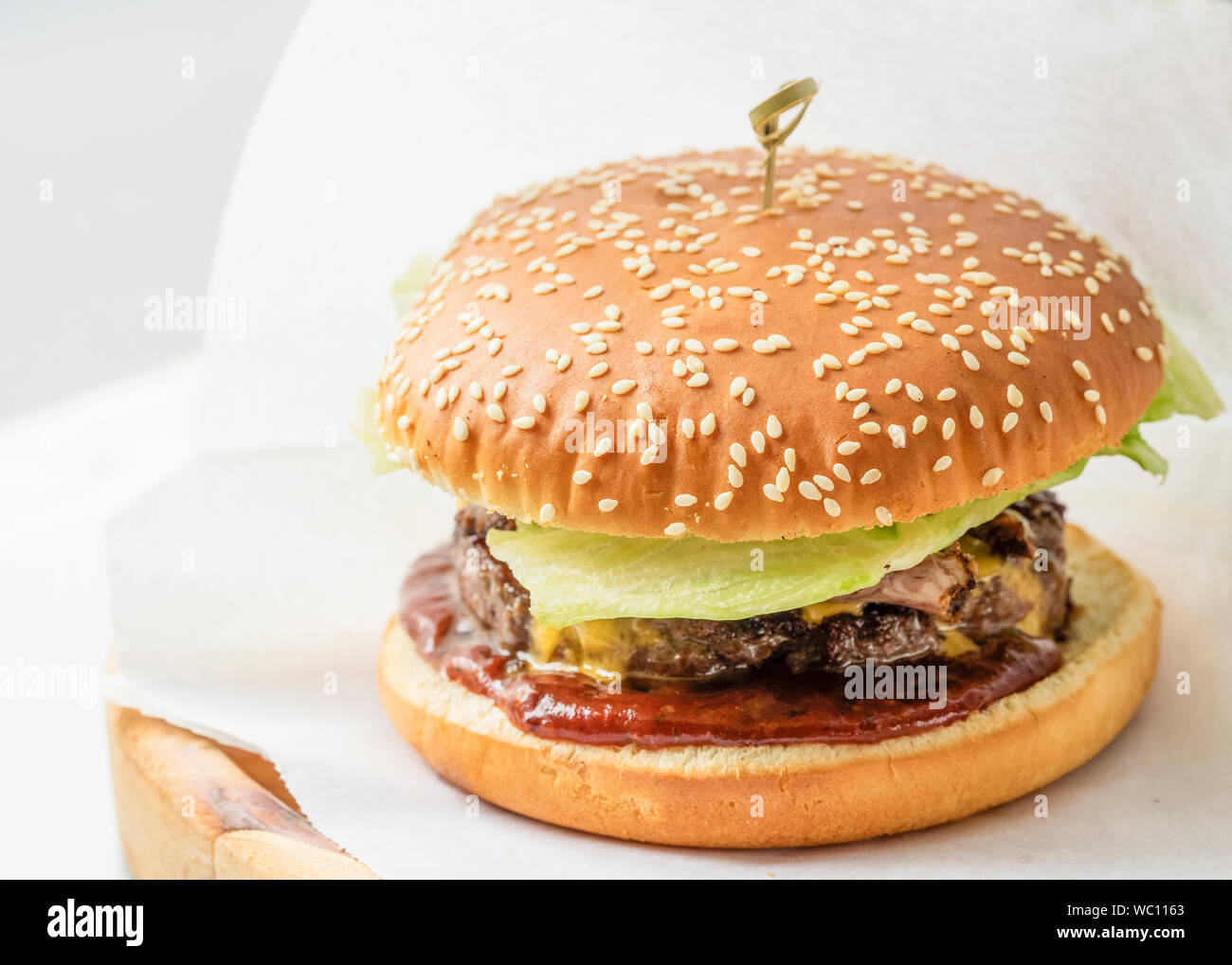 Close-up Of Fresh Burger With Camembert Cheese On White Wax Paper In Plate Stock Photo