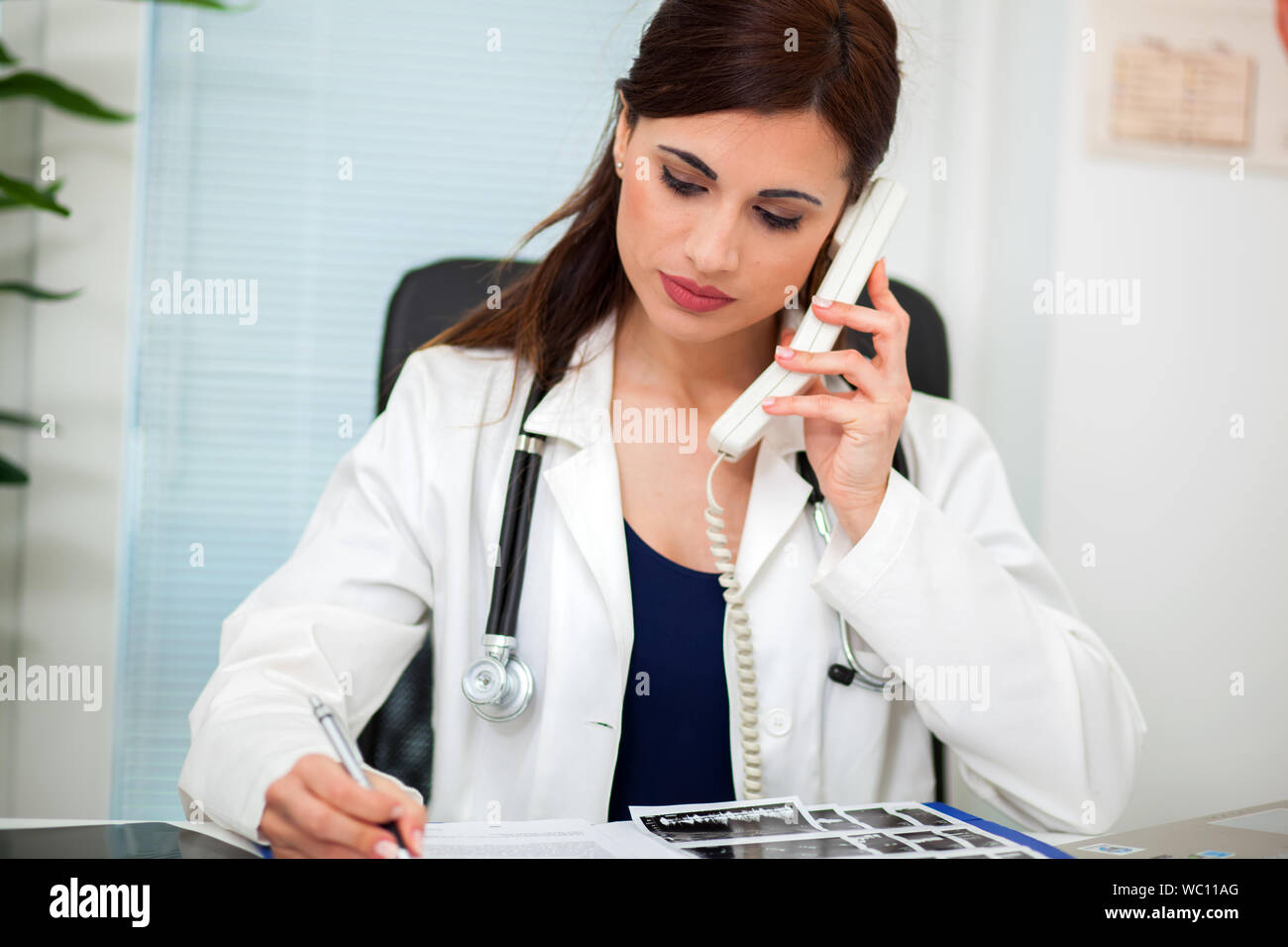 Young female doctor working at office desk and answering phone calls Stock Photo